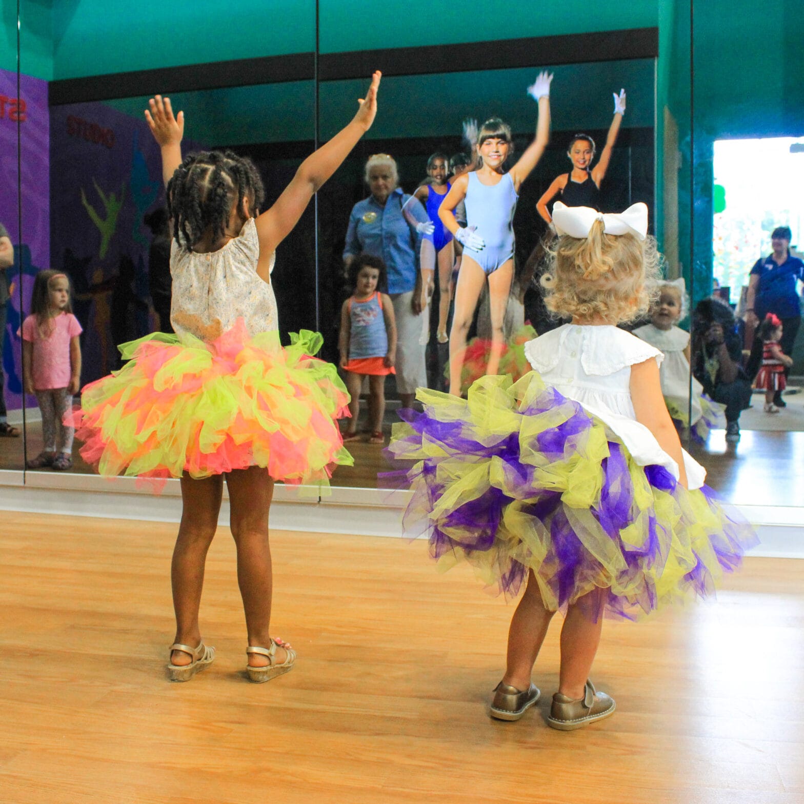Two little girls wearing multi-colored tutus dancing in front of the mirror in the BR Star Studio.