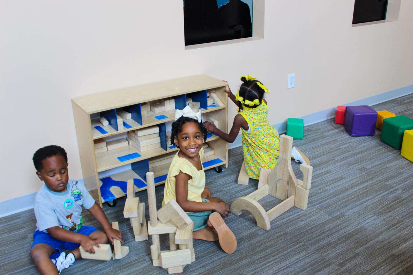 Three young children playing with building blocks and toys in the Geaux Figure Playhouse