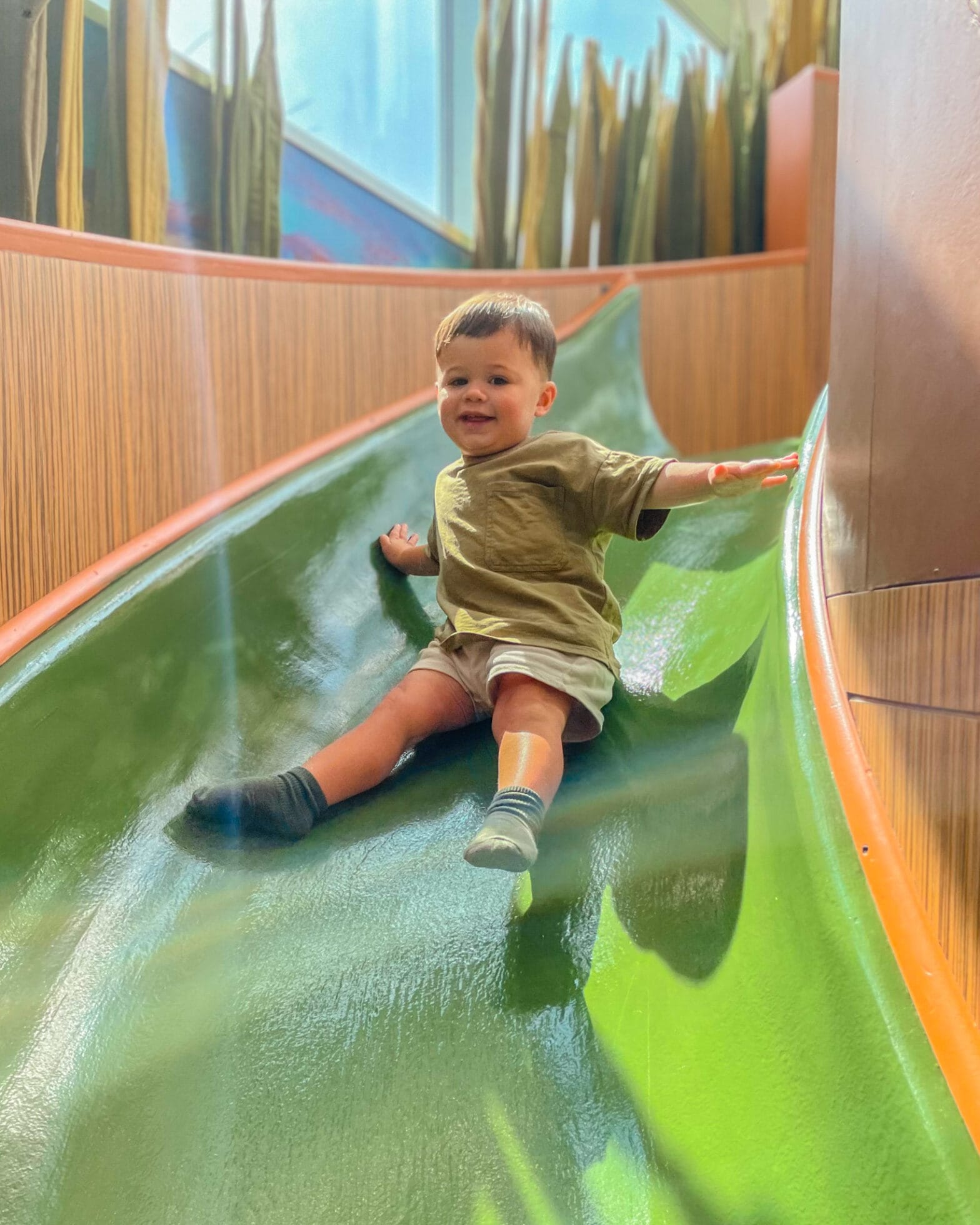 A little boy sliding down the green slide in the Crawbaby play area