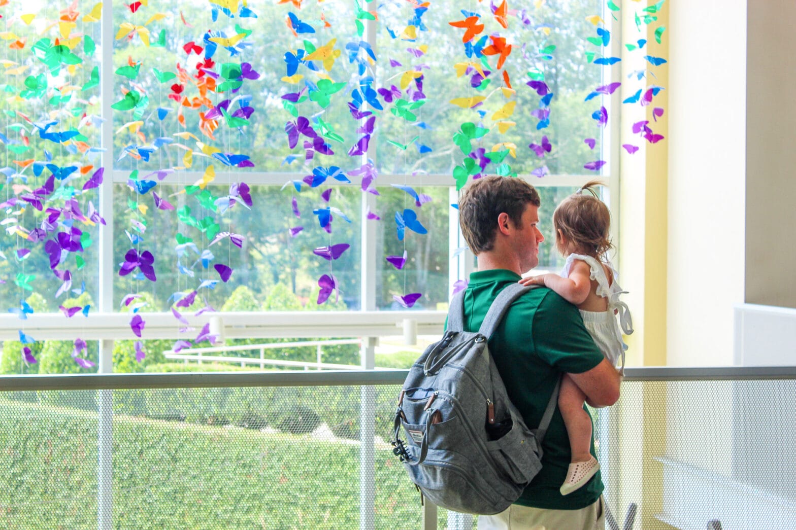 A dad carrying his child around and looking at the colorful paper butterflies