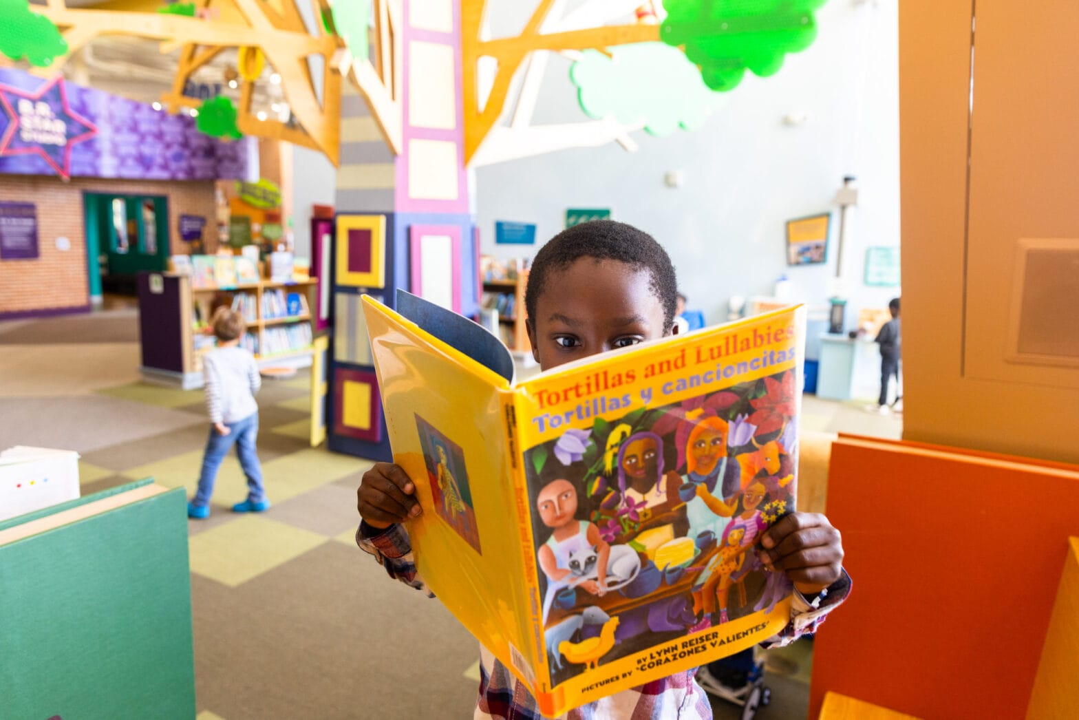 A child holding an open book and reading in the Story Tree area.