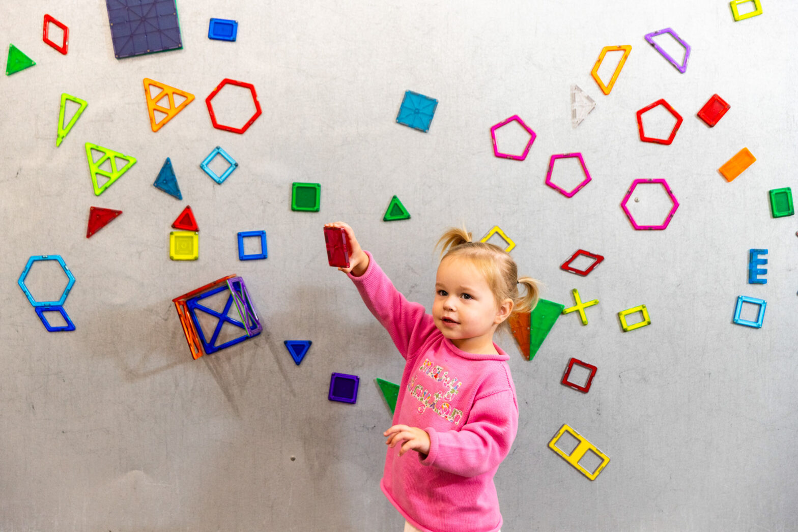 A little girl playing with shapes at the magnet wall