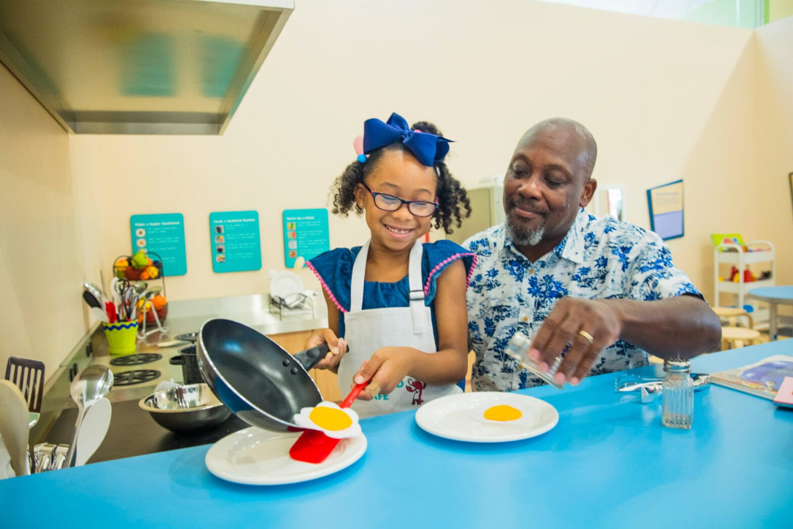 A father and daughter plating toy food in the play cafe.