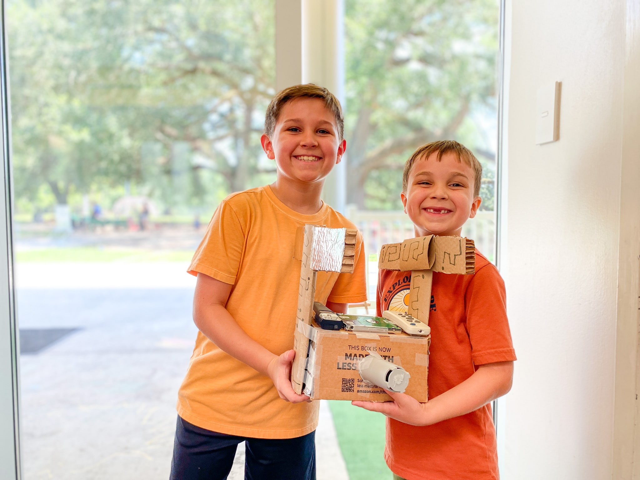 A boy and his little brother holding a castle made out of cardboard they constructed together.