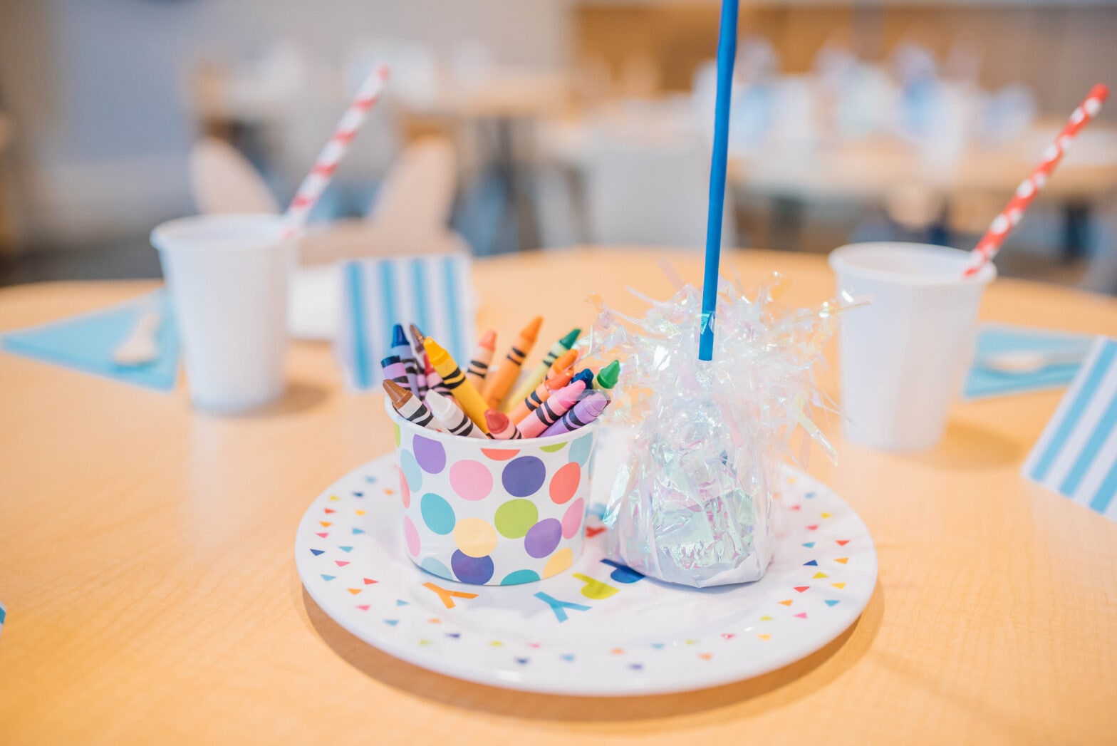 A birthday party paper plate with a party favor on top and a cup of crayons