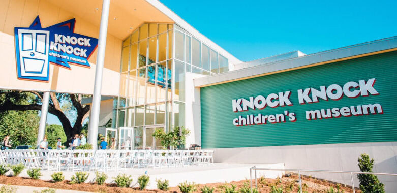 A green and yellow building with large windows with a sign that states "Knock Knock Children's Museum"