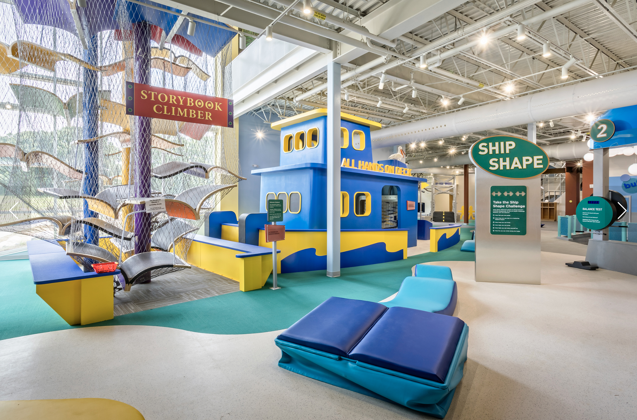 image of lower level of museum that depicts a climbing tower, a playhouse boat and exercise equipment