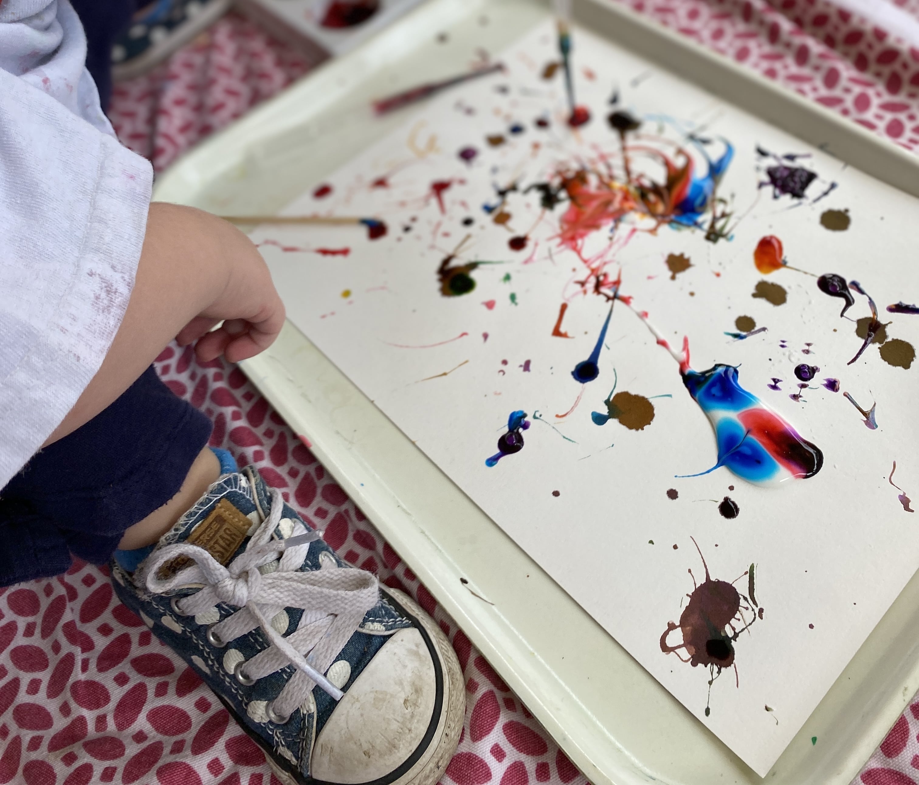 Splatter painting with various colors being done by a young child (off screen).