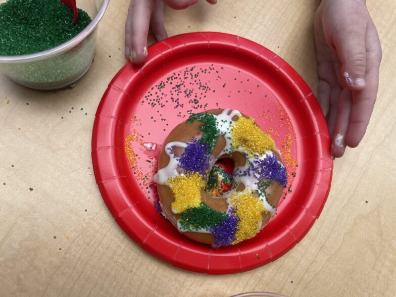 A decorated donut King Cake with purple, yellow and green sprinkles on a plate