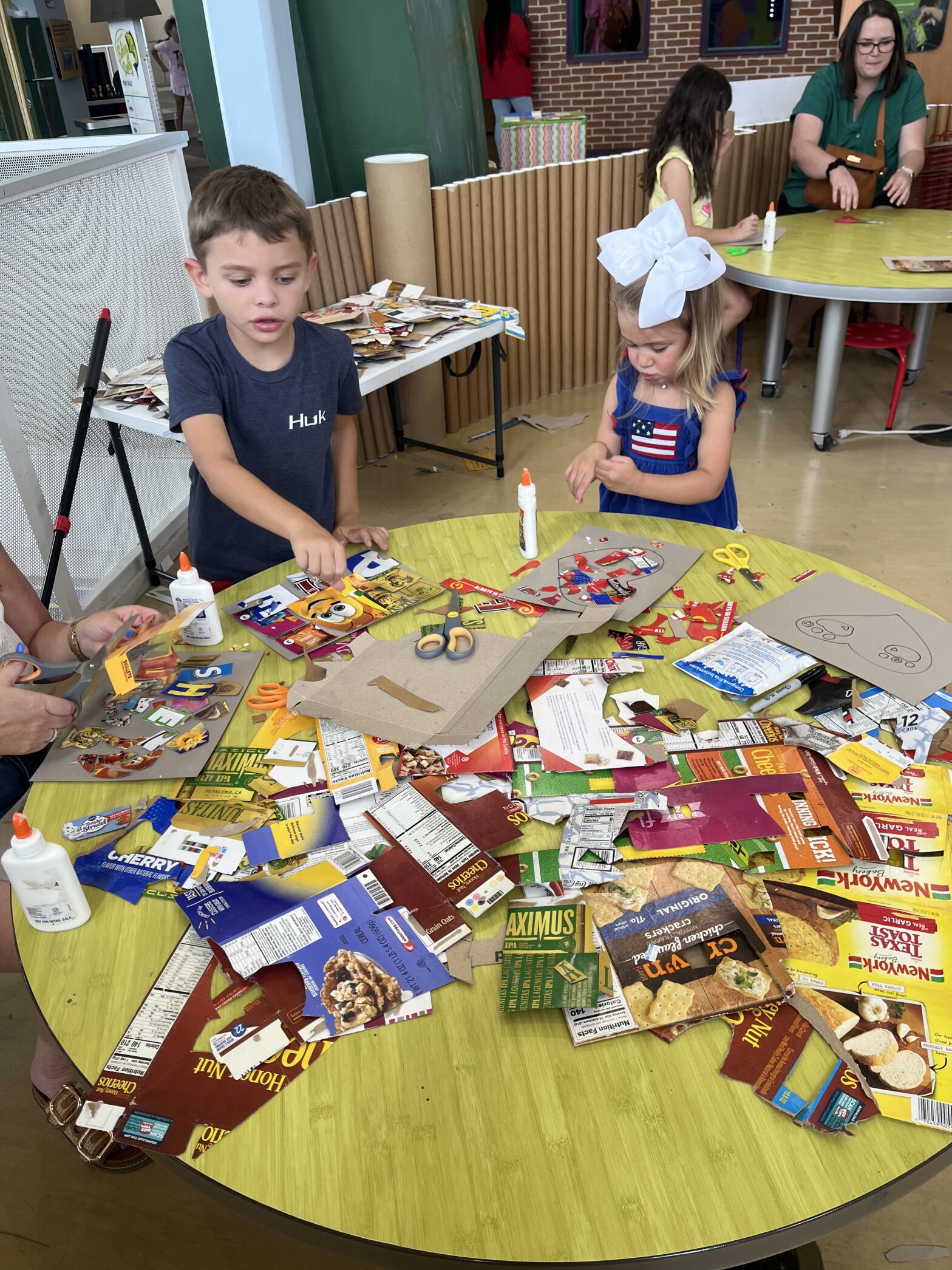 Two children create collages out of cereal boxes.